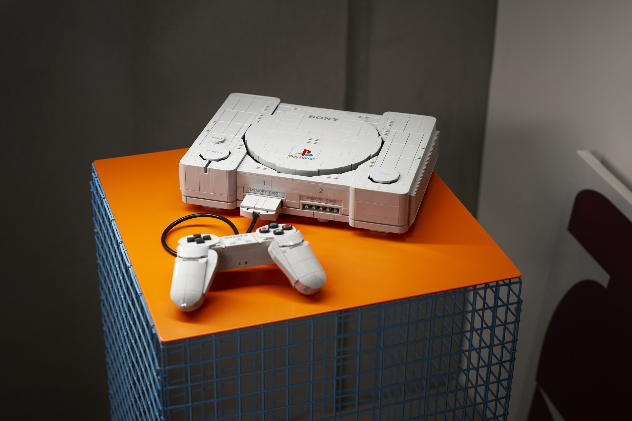 Official LEGO lifestyle still of set 72306, the brick PlayStation console and controller on an orange display. The LEGO Group.