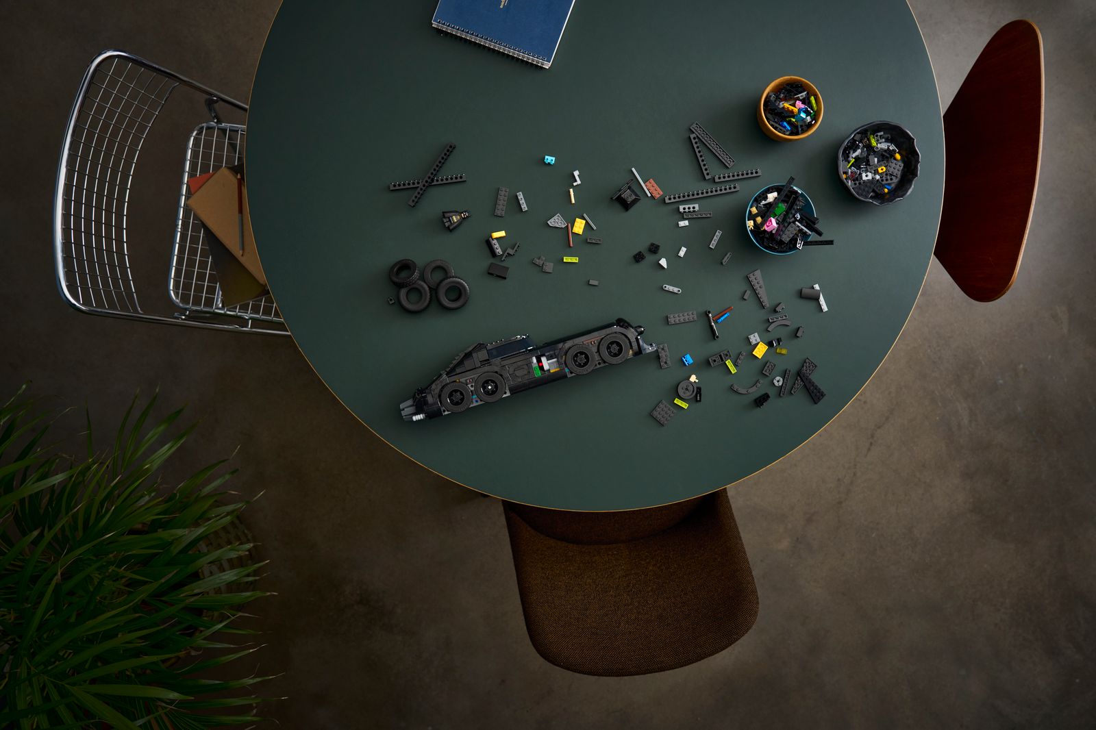 Official LEGO lifestyle still of 76355 Batman Returns Batmobile mid-build on a table with sorted elements and Batman minifigure. The LEGO Group.