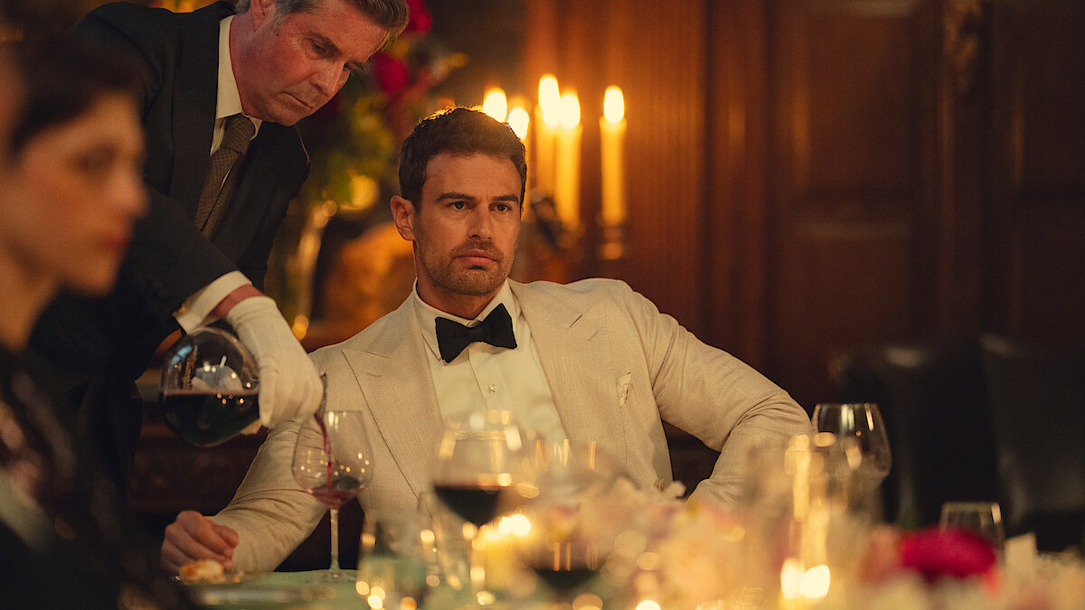 Official Netflix Tudum still from The Gentlemen Season 2: Theo James as Eddie Horniman at a candlelit dinner as wine is poured. Photo by Christopher Raphael / Netflix.